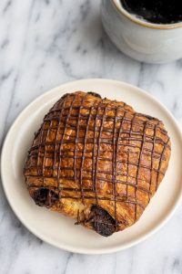 A buttery, flaky, chocolate croissant next to a cup of coffee.